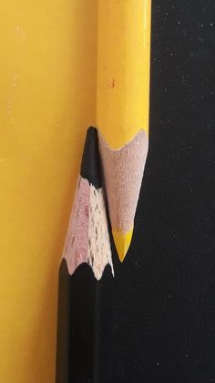 a yellow pencil sticking out of the side of a black eraser on a yellow wall