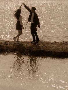 a man and woman are standing on the shore with their arms around each other as they hold hands