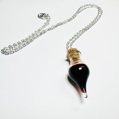 a necklace with a bottle on it sitting on a white table next to a chain