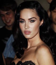 a woman with long dark hair wearing a black dress and posing for the camera while others look on