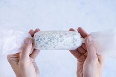 two hands holding up a piece of bread with blue cheese on it and plastic wrapper