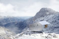 a small white building sitting on top of a snow covered mountain with mountains in the background