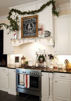 a kitchen decorated for christmas with white cabinets and black counter tops, silver appliances and holiday decorations