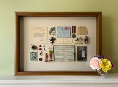 a vase filled with flowers sitting on top of a white mantle next to a framed book