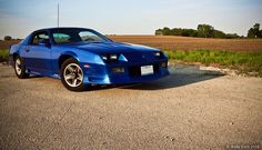 a blue sports car is parked on the side of the road in front of a field