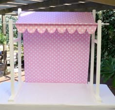 a pink and white stand with polka dot fabric on it's sides, under a pergolated roof