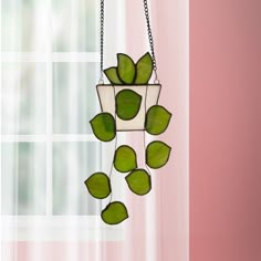 a hanging planter with green leaves in front of a pink wall and window behind it