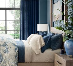 a bedroom with blue walls and white bedding, plants on the side of the bed