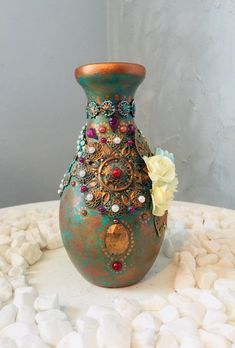 a green vase sitting on top of a white table covered in rocks and stones with flowers