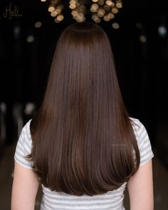 the back of a woman's head with long, straight brown hair and lights in the background