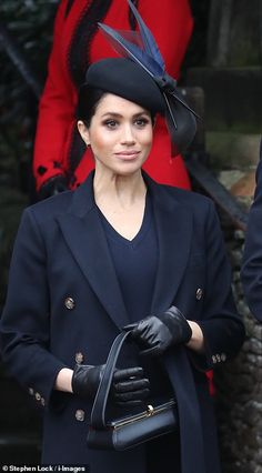 a woman in a black hat and coat holding a handbag while standing next to other people