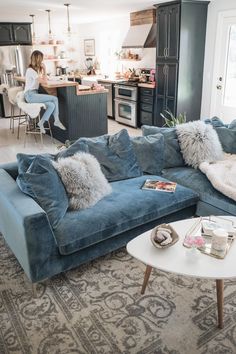 a living room filled with furniture and a woman sitting at a kitchen counter in the background