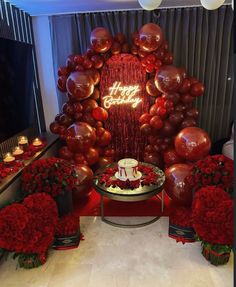 a birthday cake surrounded by red flowers and balloons in front of a large balloon arch