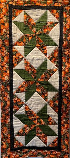 an orange and green quilted wall hanging with pumpkins on the bottom, along with black trim