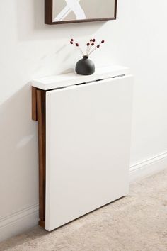 a white cabinet with a black vase on top next to a wall mounted art piece