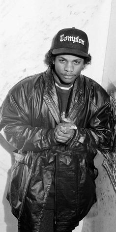 a black and white photo of a young man in a leather jacket with a hat