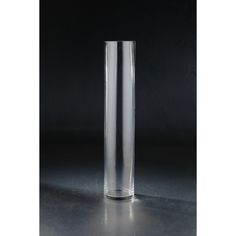 a tall clear glass vase sitting on top of a table next to a black wall