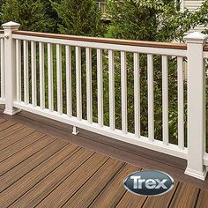 a deck with white railings and wood flooring next to trees in front of a house