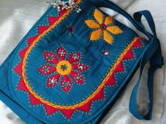 a blue bag with flowers on it sitting on a white bed sheet, next to a silver chain