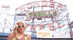 a woman wearing sunglasses standing in front of a sign for the wonder thrills ride