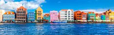 colorful buildings line the water in front of a blue sky and white cloud filled sky