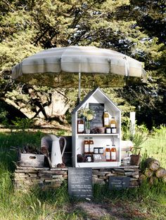 an outdoor display in the grass with bottles and jars on it's shelf under an umbrella