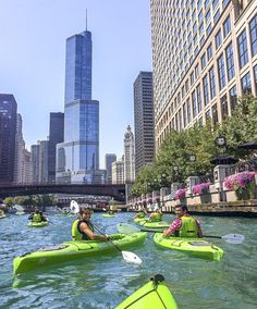 several people in kayaks paddling down the river with skyscrapers in the background