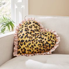 a leopard print heart shaped pillow sitting on top of a white couch next to a window