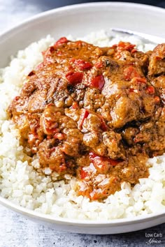 a white bowl filled with rice and meat covered in red sauce next to a fork