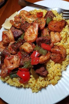 a white plate topped with rice and shrimp next to a fork on top of a wooden table