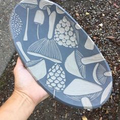 a hand holding a blue and white plate with mushrooms on it's side, in front of gravel