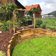 a wooden garden bed in the middle of a yard with green grass and flowers around it