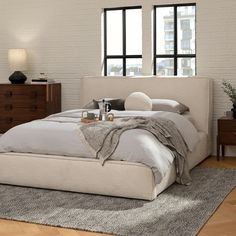 a large bed sitting next to two windows in a room with wooden floors and white walls