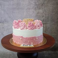 a pink and white birthday cake on a wooden stand