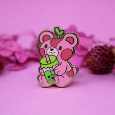 a pink teddy bear pin sitting on top of a table next to some purple flowers