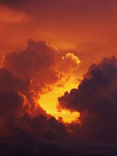 the sun is setting behind some clouds in an orange and yellow sky with dark clouds