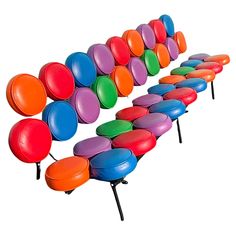 the colorful bench is made out of many different colored plastic balls and stands on black metal legs