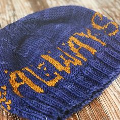 a blue hat with yellow writing on it sitting on top of a wooden table next to a cell phone