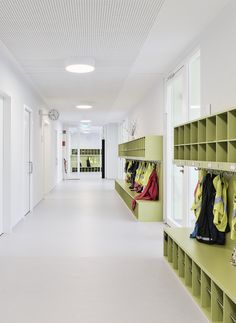 an empty hallway with green lockers and yellow jackets on the shelves in front of them