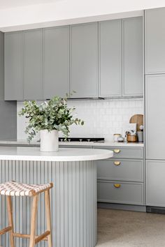 a kitchen with gray cabinets and white counter tops, an island in the middle has a plant on it