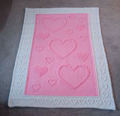 a pink and white crocheted afghan with hearts on the front, sitting on carpet