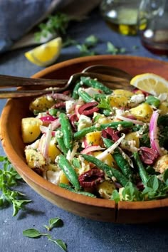 a wooden bowl filled with salad next to lemon wedges