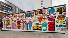 a large mural on the side of a building in front of a shopping center with people walking by