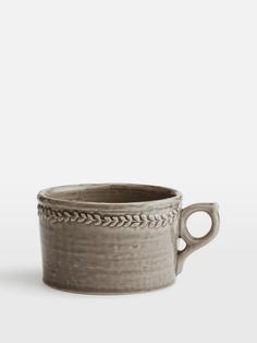 a gray cup with handles and braiding around the rim, sitting on a white surface