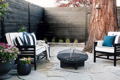 an outdoor seating area with two chairs, a fire pit and a tree in the background