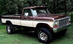 a brown and white truck parked on top of a grass covered field next to trees