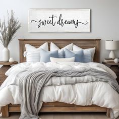 a bed with white sheets and blue pillows in a bedroom next to a wooden sign that says sweet dreams