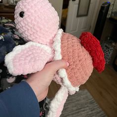 a person holding two small stuffed animals in their hands, one is pink and the other is red