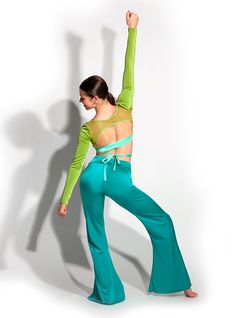 a woman in green and blue pants is dancing with her arms up to the side