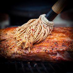 a large piece of meat being cooked on the grill with a brush attached to it